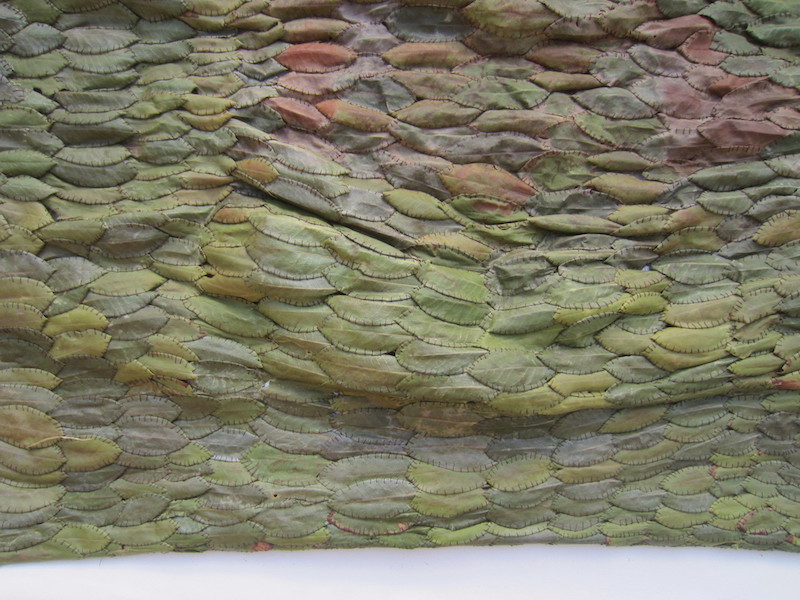 A close-up view of leaves in many shades of green painstakingly sewn together into a kind of draping textile.